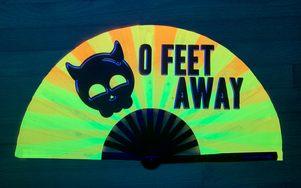 Black print 0 Feet away bamboo hand fan by fabulous me fans on Gold and yellow UV fabric glowing under UV light. For circuit parties, raves, and festivals.